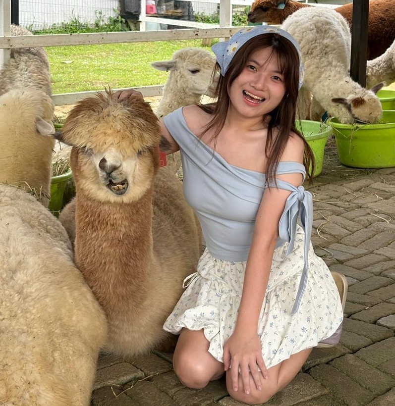 Teh Ming En smiling while sitting next to an alpaca.